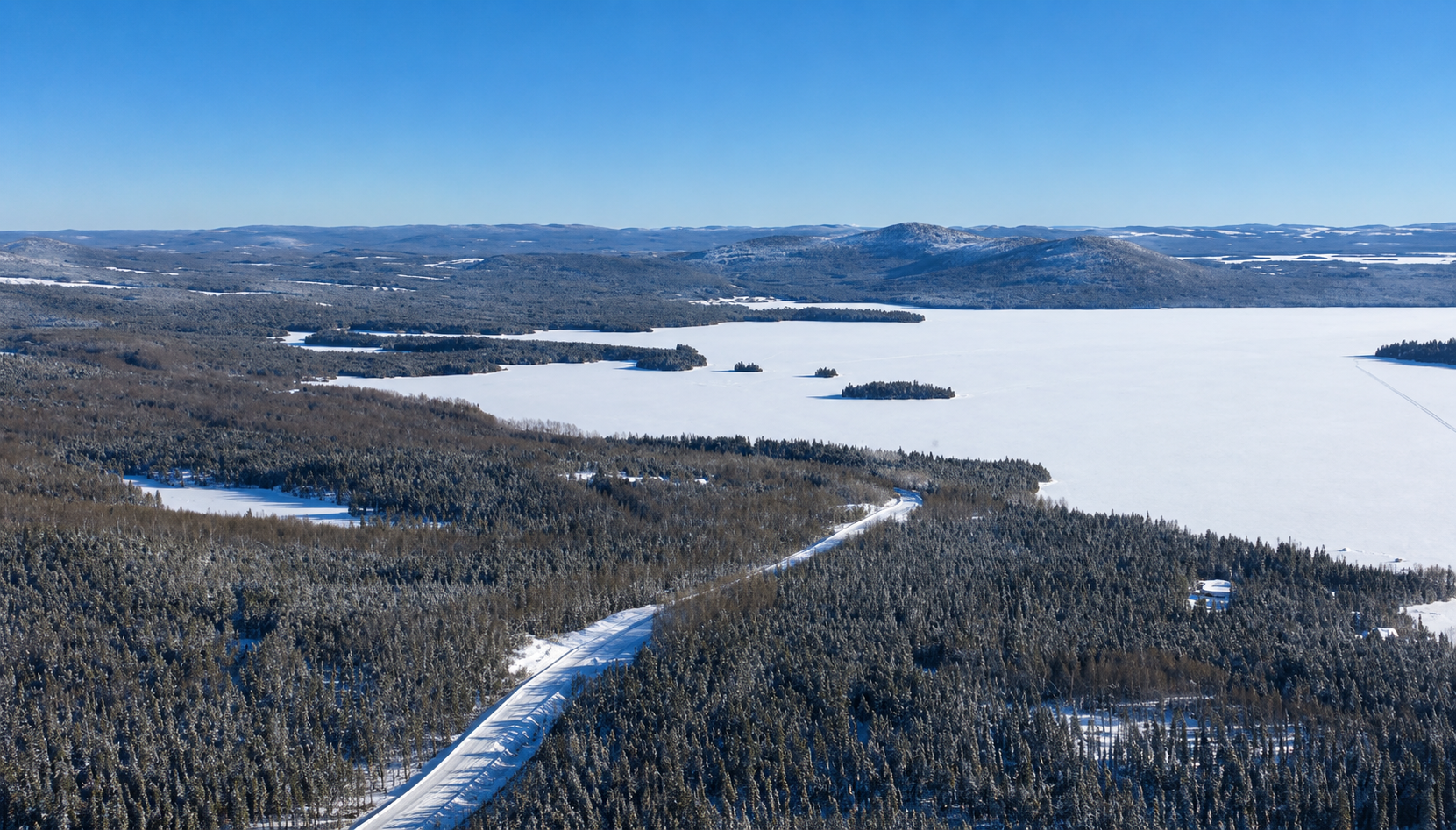 Aerial view of the Mont Sorcier magnetite project in Canada with terraced open-pit benches, haul roads and processing pond set against forested mountains